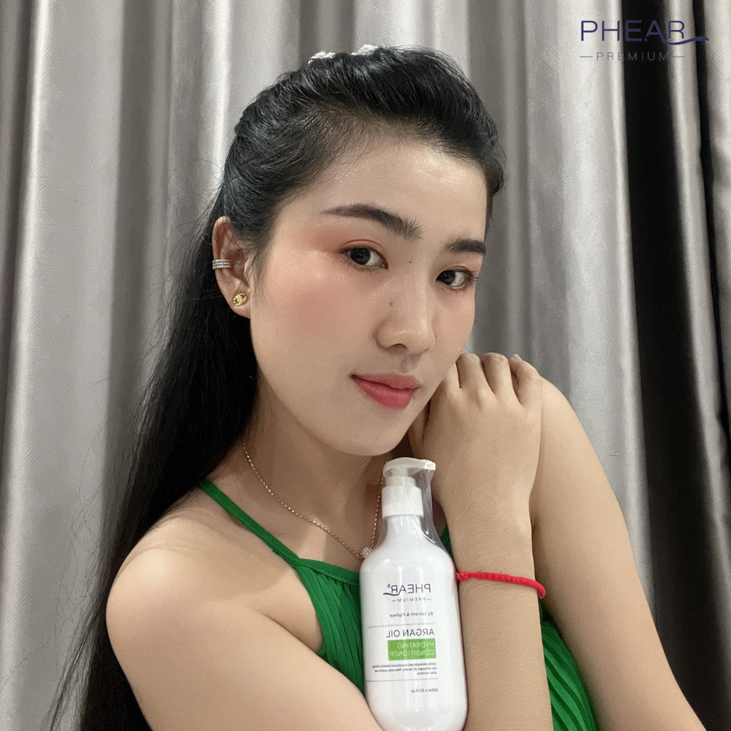 Woman holding a bottle of PHEAR hydrating conditioner against a gray curtain background