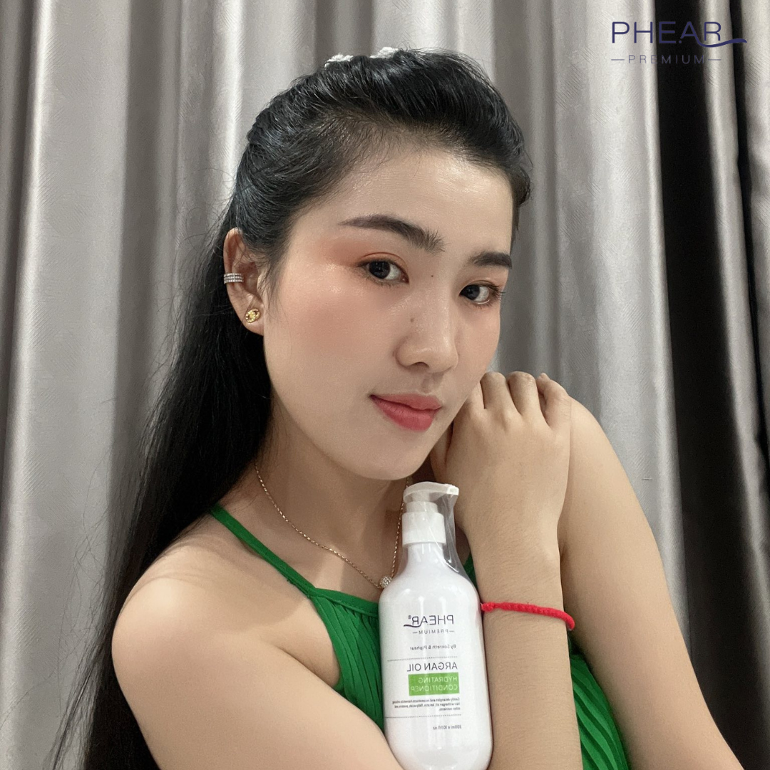 Woman holding a bottle of PHEAR hydrating conditioner against a gray curtain background