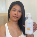 Woman holding a bottle of PHEAR shampoo against a neutral background