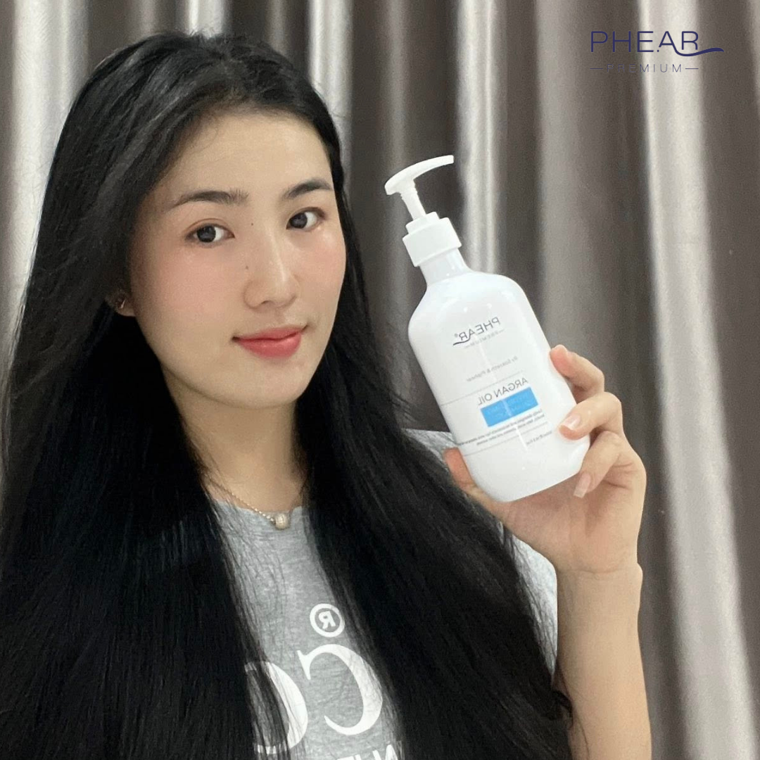 Woman holding a white bottle with a pump, branded 'PHEAR', against a neutral background.